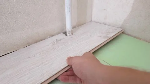 Worker hand laying laminate flooring around a pipe Stock Footage 326150242