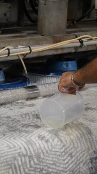 Worker hand pouring liquid from clear measuring jug beside industrial floor Stock-Fotos