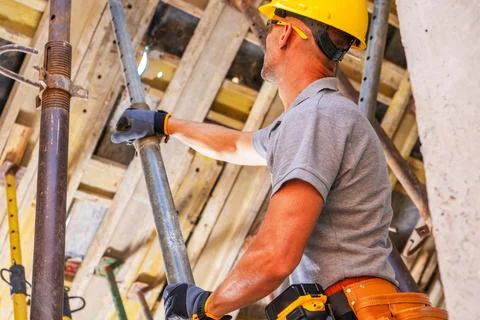 Worker handling an adjustable steel prop under roof framing Photos