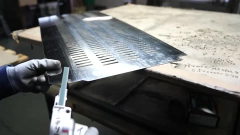 Worker handling perforated metal sheet and operating press brake machine in Stock Footage 345013225