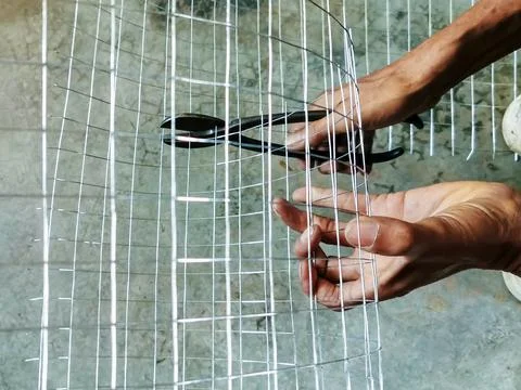 Worker hands cutting wire mesh with pliers on concrete floor. Hands using w.. Stock Photos