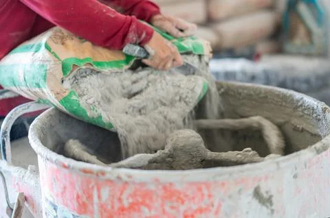 Worker hands emptying a bag of dry mortar mix into an active cement mixer d.. Stock Photos