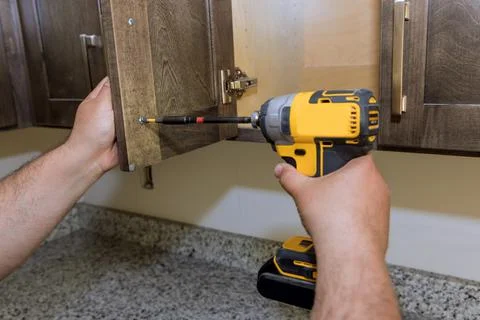 Worker hands fixing a hinge to a kitchen cabinet Stock Photos