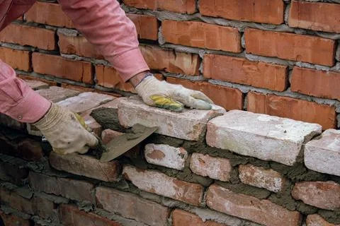 Worker hands laying bricks with mortar during wall construction Stock Photos