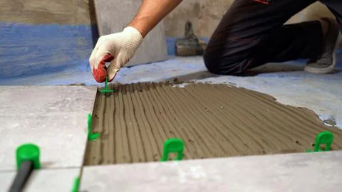 Worker hands placing spacers between ceramic floor tiles. Installing a large  Stock Photos