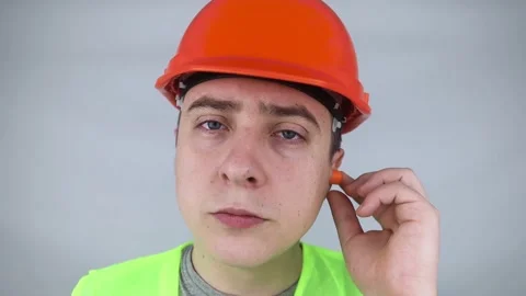 A worker in a hard hat and green vest puts on ear plugs. Industrial safety. Indu Stock Footage 187968564