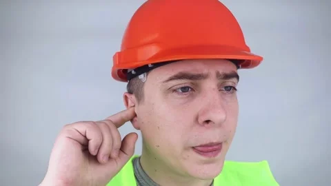 A worker in a hard hat and green vest puts on ear plugs. Industrial safety. Indu Stock Footage 187968687