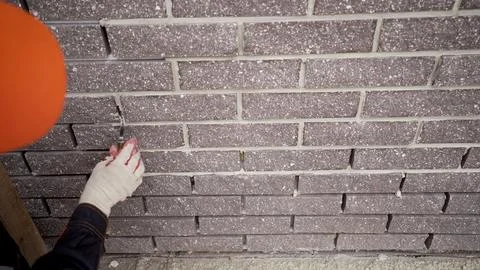 Worker in a hard hat applying grout to a decorative brown brick wall during.. Stock Photos