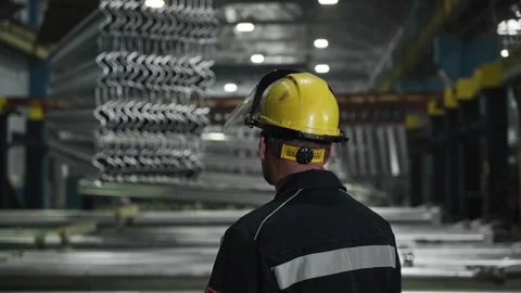 A worker in a hard hat in a large factory. Heavy steel parts are suspended from Video stock 297178145