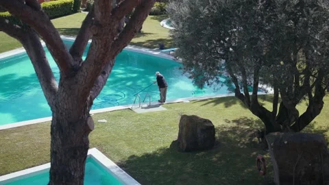Worker in a hat cleans the pool. Light ripples and sun glare on turquoise water Stock Footage 154715532