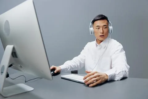 Worker in headphones at the table in front of the computer Gray background Foto stock