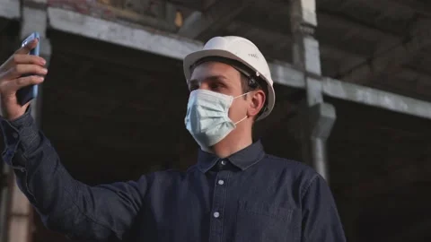Worker in helmet and mask is at facility, communicates via video communication Stock Footage 138075171