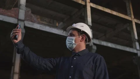 Worker in helmet and mask is at facility, communicates via video communication Stock Footage 138081573