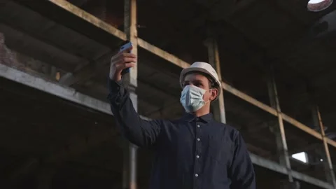 Worker in helmet and mask is at facility, communicates via video communication Stock Footage 138087874