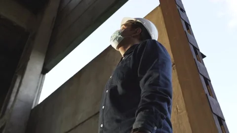 A worker in a helmet at a construction site puts on a protective mask Stock Footage 138245461