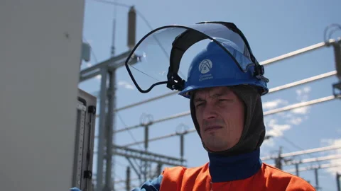 Worker in helmet with logo fixes switchboard at substation Stock Footage 156318388