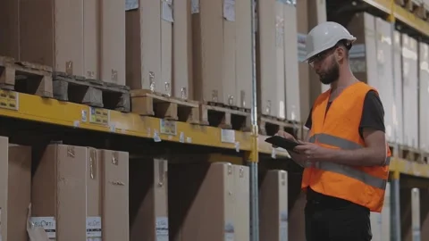 Worker in a helmet in a warehouse. The warehouse manager inspects the warehouse Stock Footage 296319755