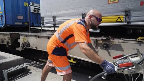 A worker in high-visibility clothing connecting a cable to a train set Stock Footage 338371711