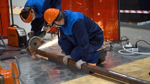 Worker hold metal pipe, use power tool to saw off with grinder. Fenced area. Stock Footage 126357378