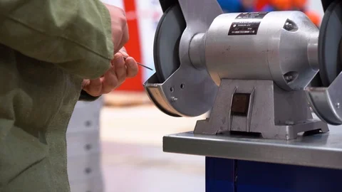 Worker hold thin metal rod, carefully polishes sharp object on grinding machine Stock Footage 126356600