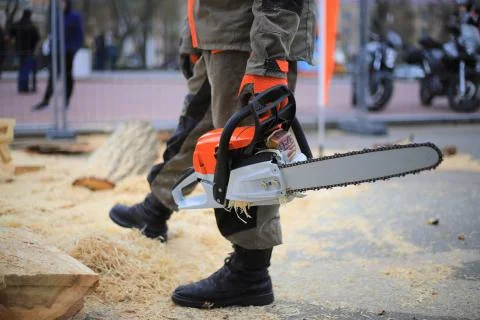 Worker holding a chainsaw close up on a background of wood shavings 库存照片