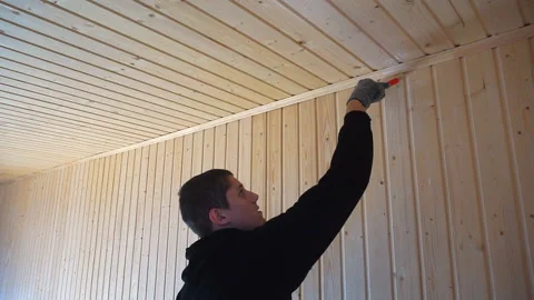 Worker holds a brush and draws a wooden wall, wall cladding, floor or wall surfa Video stock 98004441