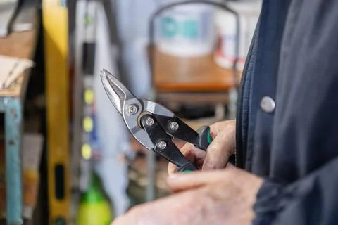A worker holds a sharp metal tin snip tool for cutting sheet steel in a Stock Photos