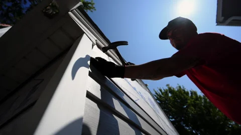 Worker hummers a nail into plastic panel siding on the outside wall of the Stock Footage 318992768
