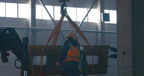 A worker inside a hangar under construction puts fabric slings on a crane hook  Stock Footage 147599559