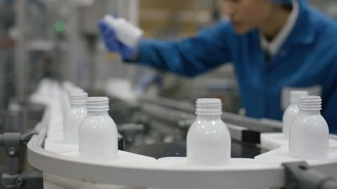 Worker inspecting cosmetic bottles moving on conveyor belt in factory Stock Footage 107975216