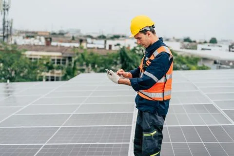 Worker inspecting solar panels on a rooftop in an urban setting during an o.. Stock Photos