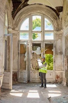 Worker inspects old building with broken windows and peeling walls Stock Photos