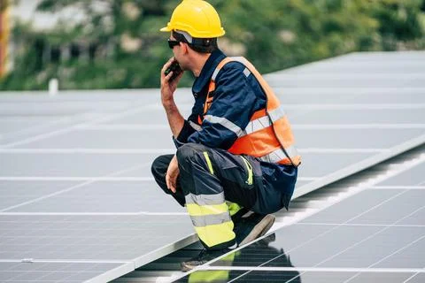 Worker inspects solar panels on a rooftop during daylight to ensure proper .. Stock Photos