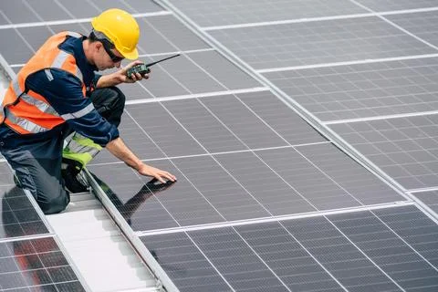 Worker inspects solar panels on rooftop while communicating with team durin.. Stock Photos