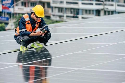 Worker inspects solar panels on a rooftop during daylight in an urban setting Foto stock