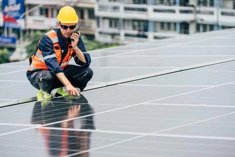 Worker inspects solar panels on rooftop in urban setting during daylight Stock Photos
