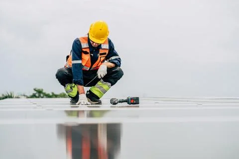 Worker inspects solar panels on rooftop while wearing safety gear and using.. Foto stock