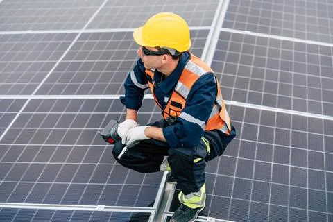 Worker inspects solar panels on a rooftop in bright daylight, focusing on r.. Stock Photos