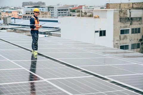 Worker inspects solar panels on rooftop in urban setting during sunny day Stock Photos