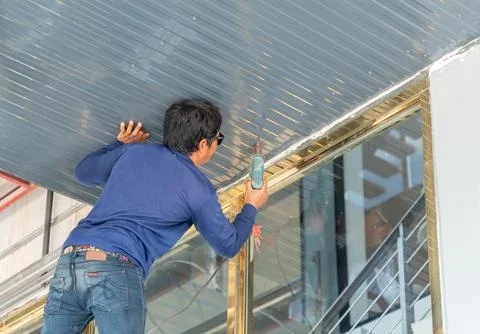 Worker install metal sheet ceiling in building. Stock Photos