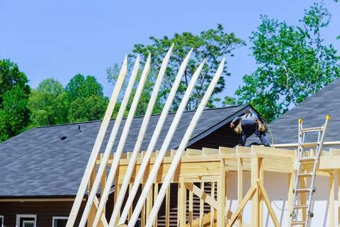 Worker installing beams using an air hammer while nailing wooden plank frames Foto stock