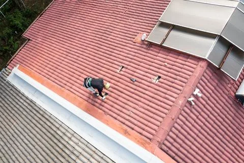Worker installing brackets onto red roof trusses for solar photovoltaic or PV Stock Photos