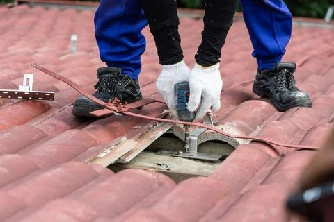 Worker installing brackets onto red roof trusses for solar photovoltaic or PV Stockfoto's