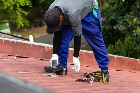 Worker installing brackets onto red roof trusses for solar photovoltaic or PV Stockfoto's