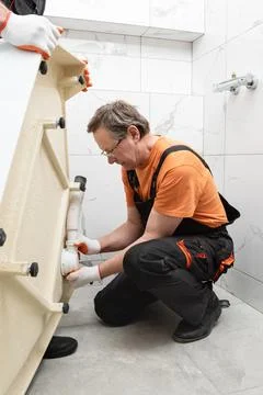 The worker is installing a drain siphon on a shower tray in the bathroom. Stock Photos