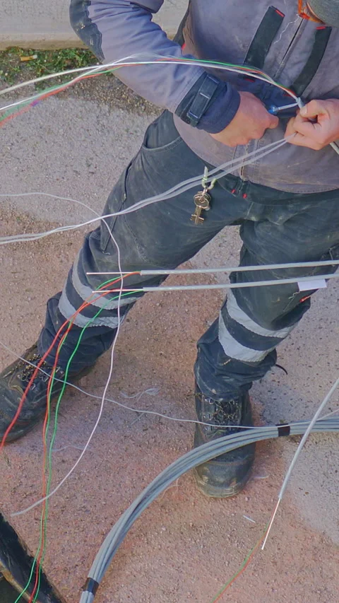 Worker installing fiber optic cables near an open utility box, wearing protec Stock-Footage 297088433