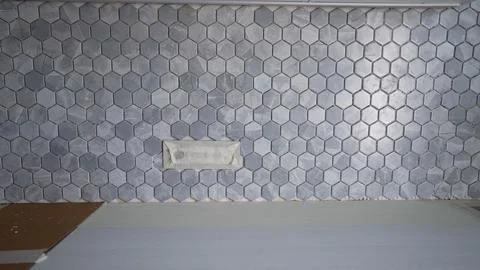 Worker installing gray hexagonal tiles on wall in bathroom Stock Photos