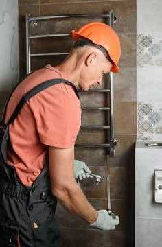 The worker is installing a heating element in the towel warmer. Stock Photos