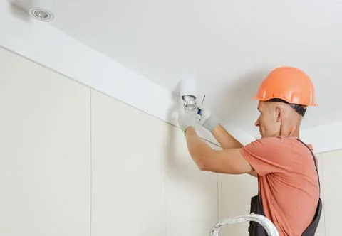 A worker is installing an LED spotlight on the ceiling. Stock Photos