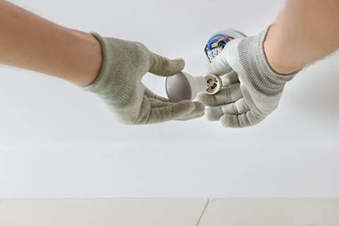 A worker is installing an LED spotlight on the ceiling. Stock Photos